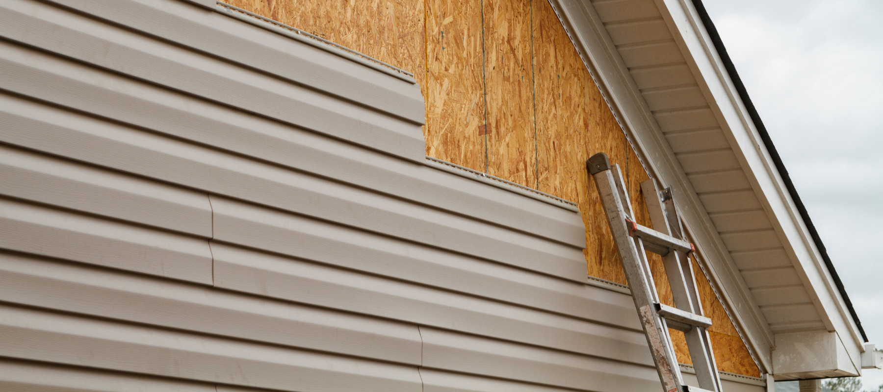 Beige vinyl siding being installed to a house.